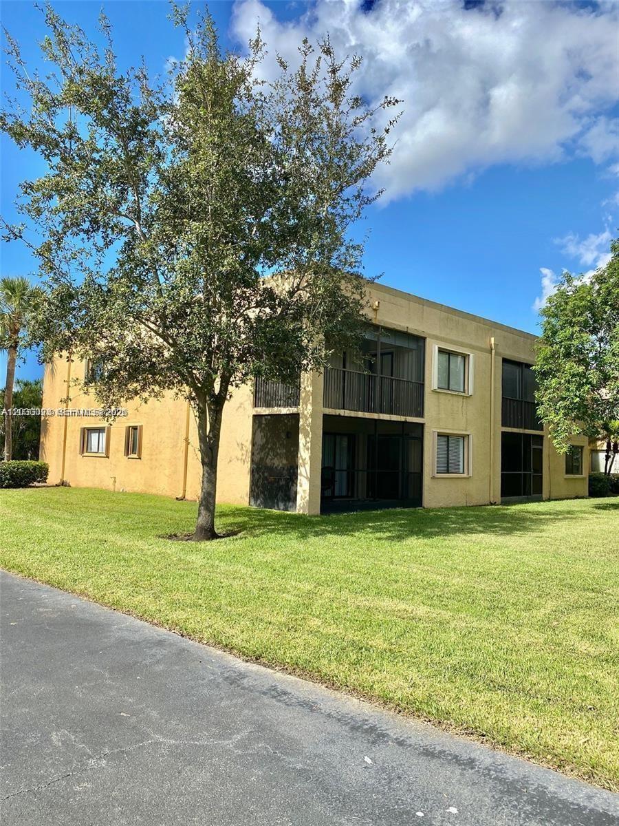 A two-story tan apartment building features screened balconies and a large tree in front — WESTON, FL