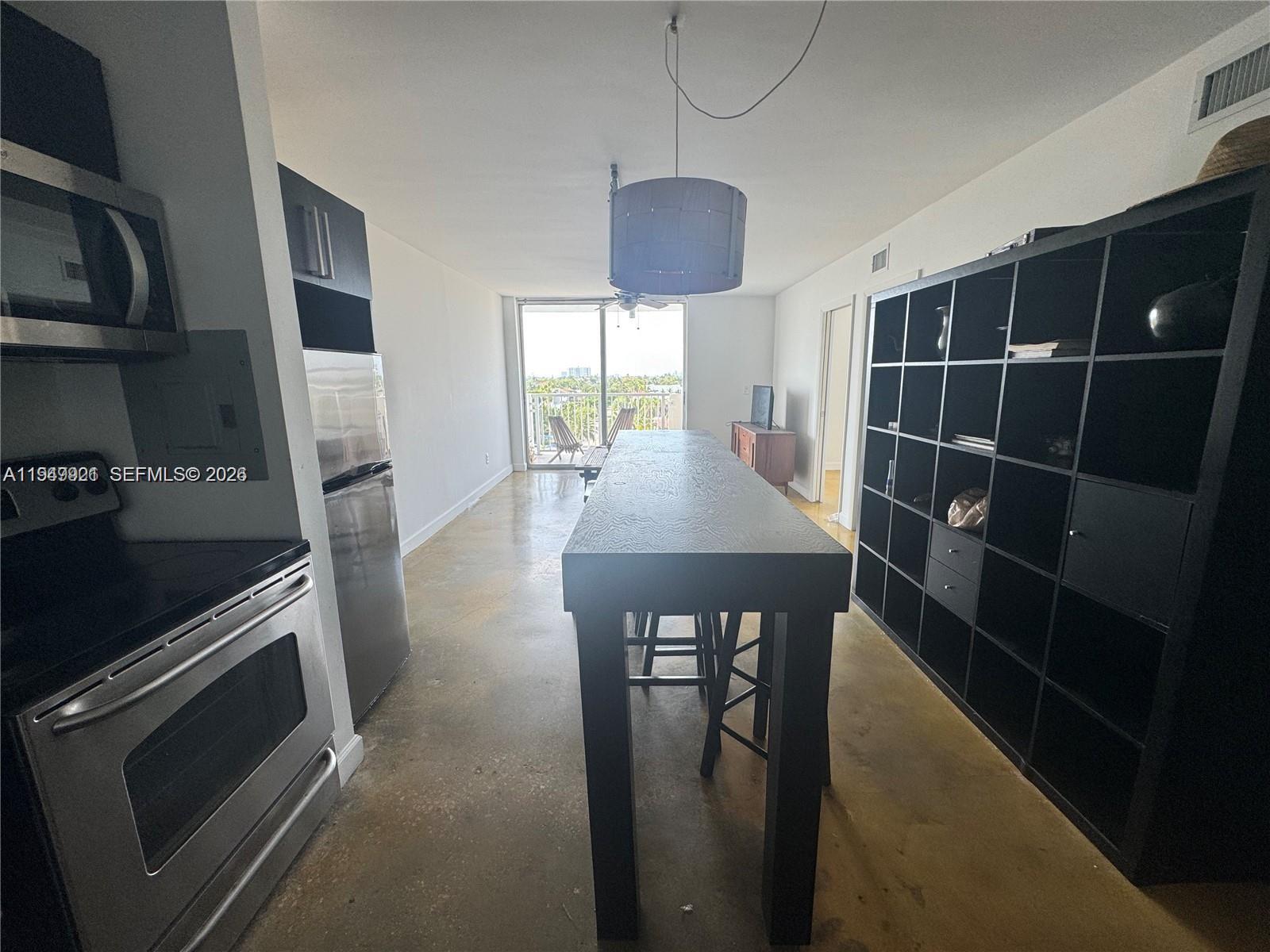 A kitchen and dining area features a long table, concrete floors, and a balcony view — 2000 NE 135th St # 606, North Miami FL 33181, NORTH MIAMI, FL