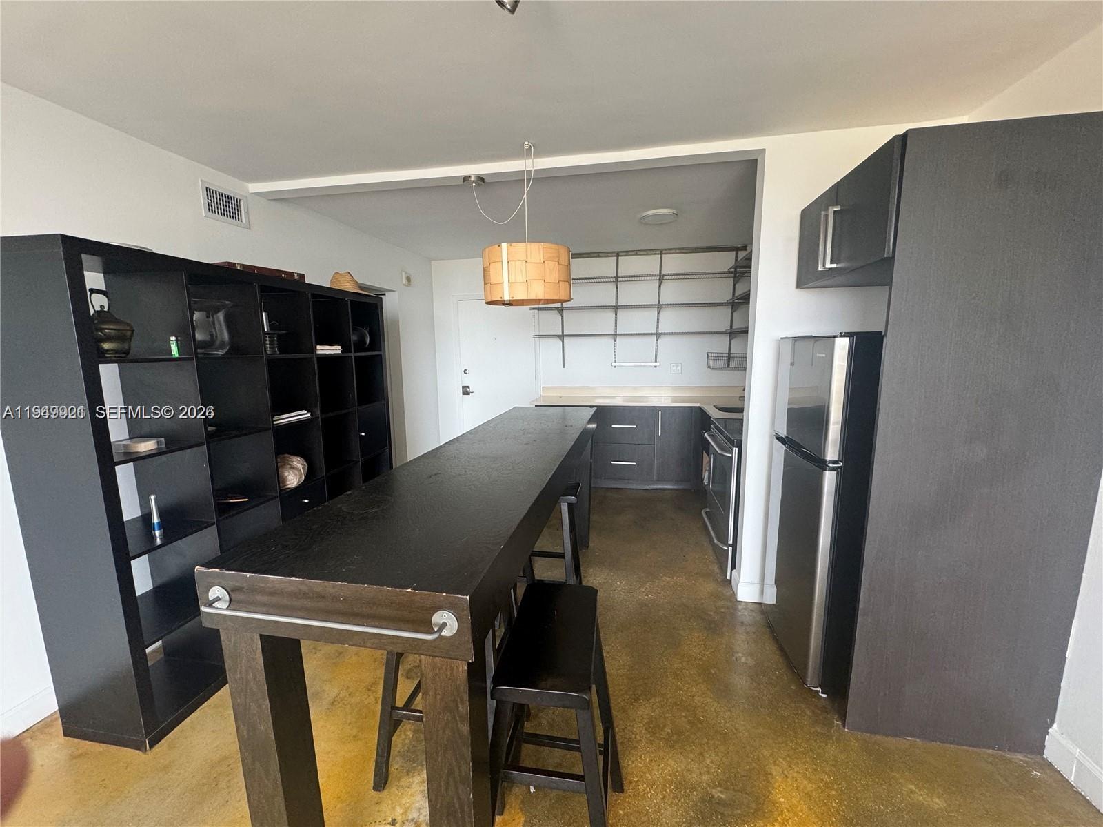 This kitchen features dark cabinetry, a long dining table, and open metal shelving — 2000 NE 135th St # 606, North Miami FL 33181, NORTH MIAMI, FL