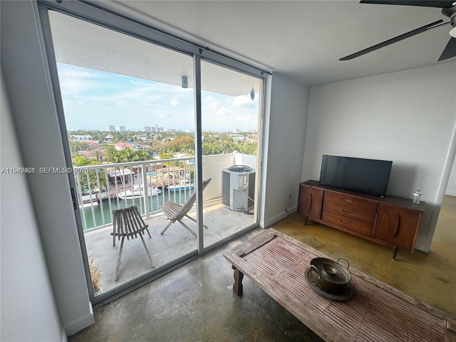 A living room with concrete floors features a wooden media console and a balcony view — 2000 NE 135th St # 606, North Miami FL 33181, NORTH MIAMI, FL