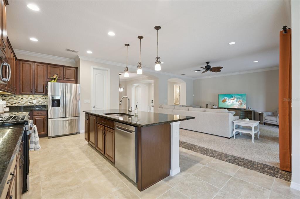 A kitchen with dark wood cabinets and a granite island opens into a carpeted living room — 588 AUTUMN ASH DRIVE, CLERMONT, FL