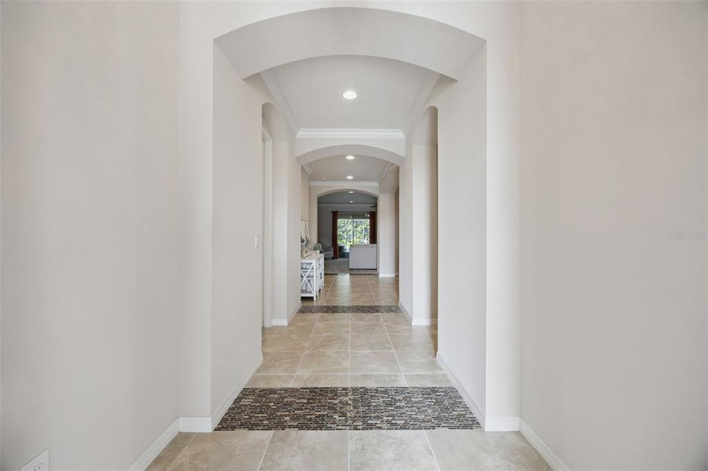 A long hallway with arched ceilings, beige tile flooring, and decorative mosaic tile accents — 588 AUTUMN ASH DRIVE, CLERMONT, FL