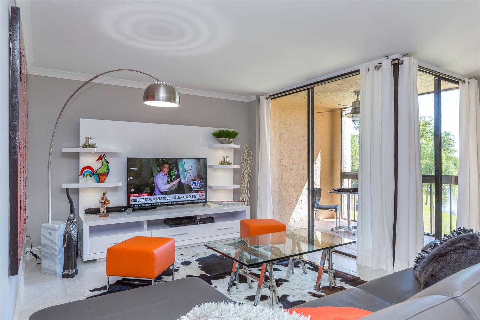 A living room features a white media console, orange ottomans, a glass table, and balcony access — 2455 Lindell Boulevard # 3304, Delray Beach FL 33444, DELRAY BEACH, FL