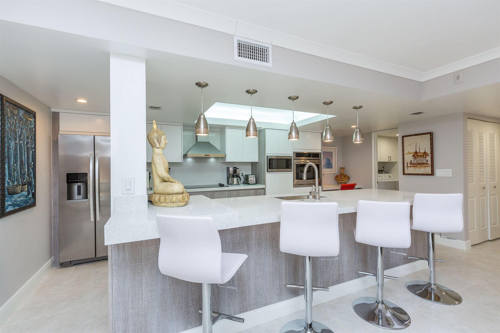 A modern kitchen features a white quartz island with three stools and stainless steel appliances — 2455 Lindell Boulevard # 3304, Delray Beach FL 33444, DELRAY BEACH, FL