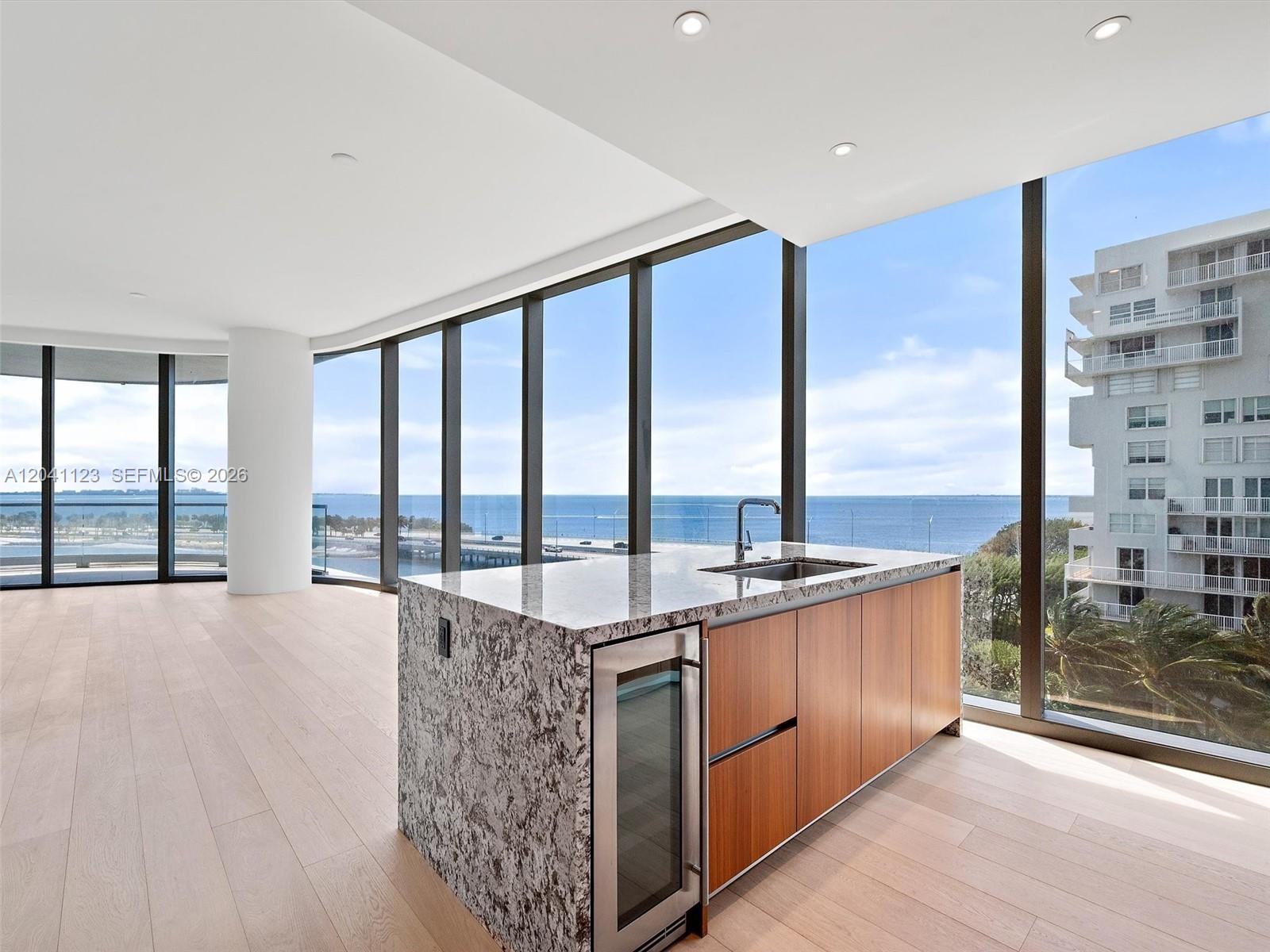 A kitchen island with a wine cooler and sink sits in a room with floor-to-ceiling windows — 175 SE 25th Rd # 502, Miami FL 33129, MIAMI, FL