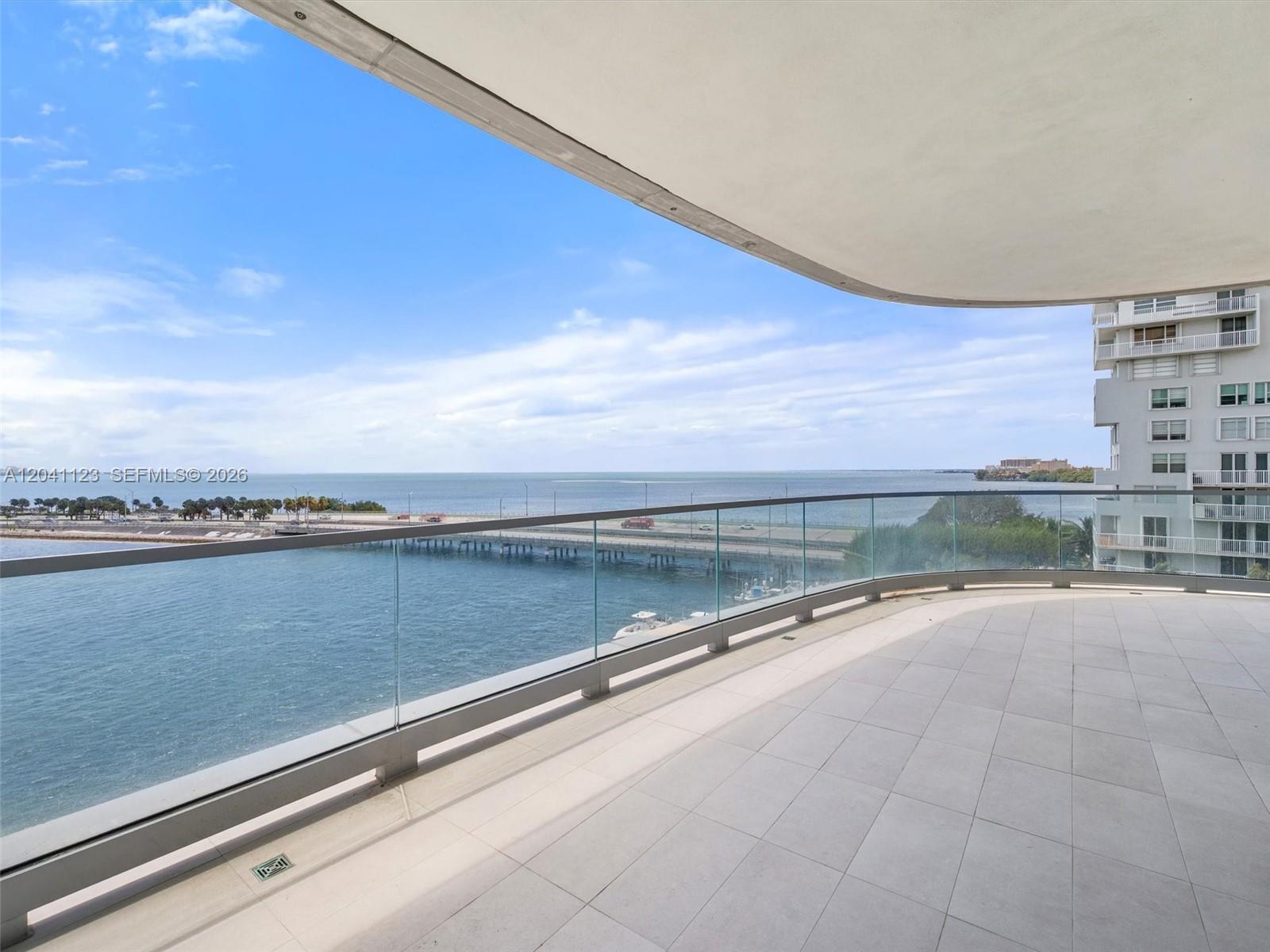 A spacious balcony with glass railings overlooks a bridge, the ocean, and a neighboring building — 175 SE 25th Rd # 502, Miami FL 33129, MIAMI, FL