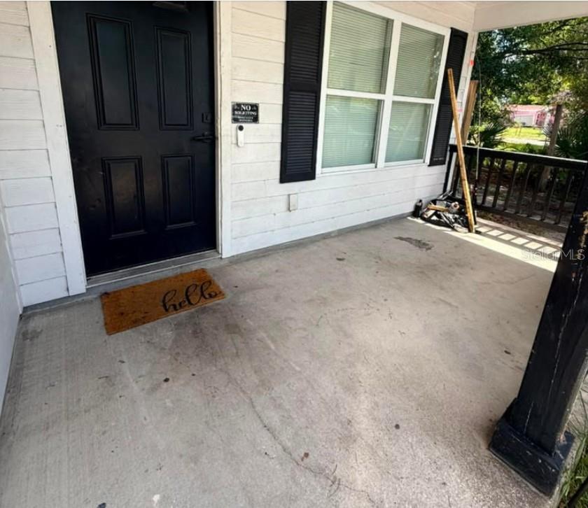 A concrete front porch features a black door, a hello mat, and a wooden railing — 323 W 9TH STREET, LAKELAND, FL