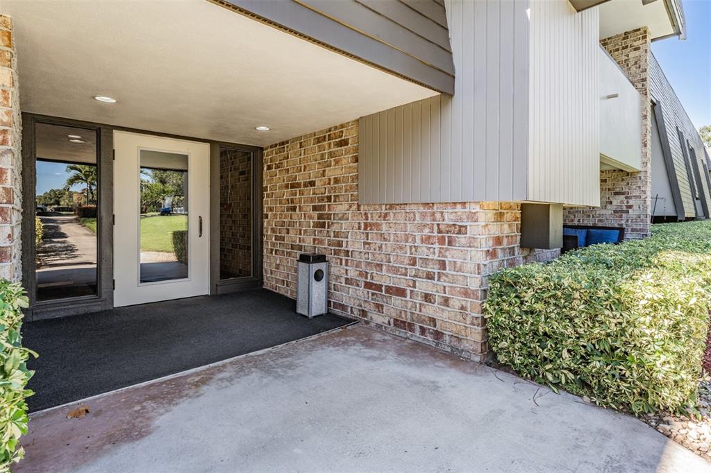 A white glass-paneled door sits under a covered entryway with brick walls and concrete flooring — 36750 US HIGHWAY 19 N UNIT 6-214, PALM HARBOR, FL