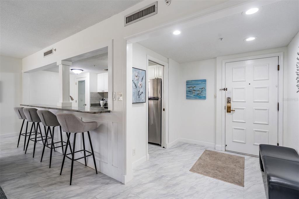 A kitchen pass-through with bar seating overlooks a tiled entryway featuring a white front door — 36750 US HIGHWAY 19 N UNIT 6-214, PALM HARBOR, FL