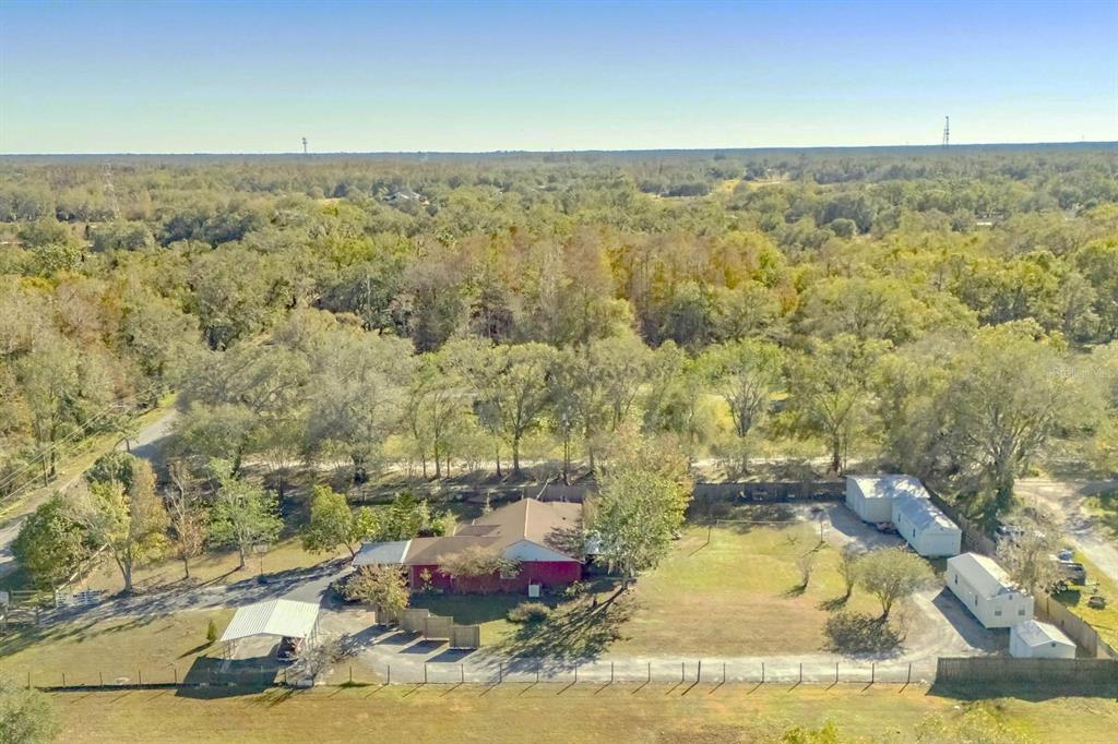 An aerial view shows a red house with a carport and outbuildings on a wooded lot — 5201 PLESS ROAD, PLANT CITY, FL