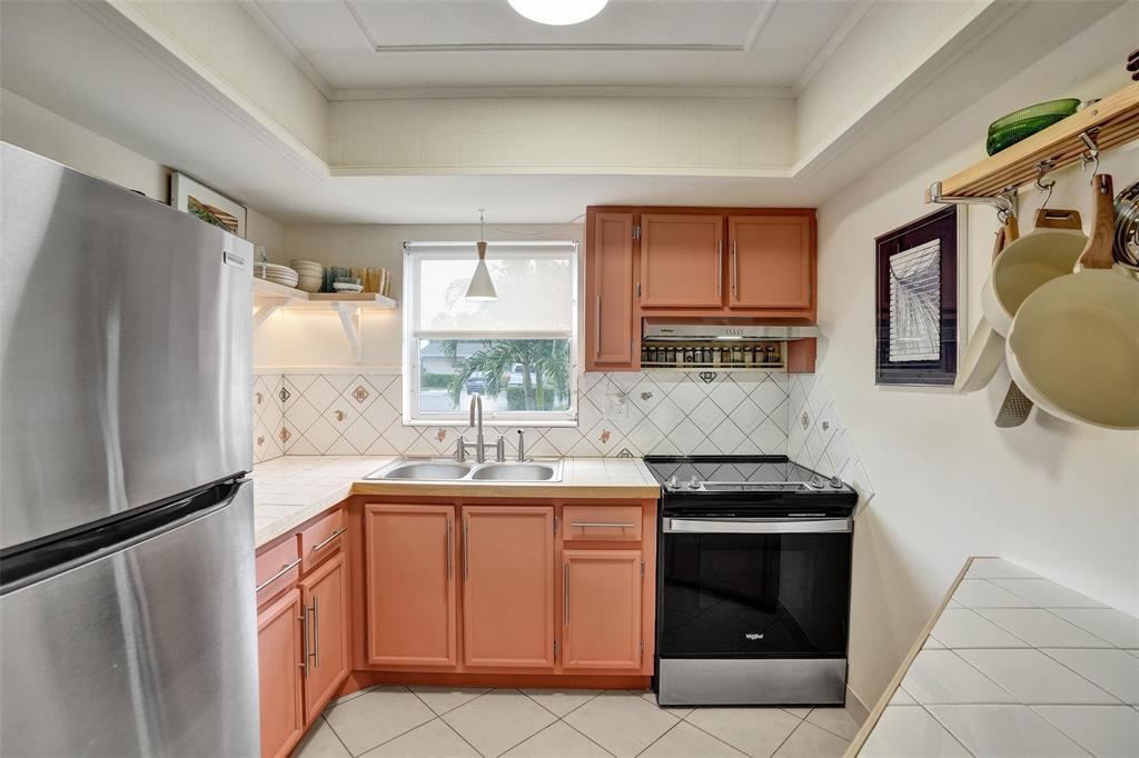 A kitchen features peach-colored cabinets, a stainless steel refrigerator, a range, and tiled countertops — 2592 E Dudley Dr Drive E # A, West Palm Beach FL 33415, WEST PALM BEACH, FL