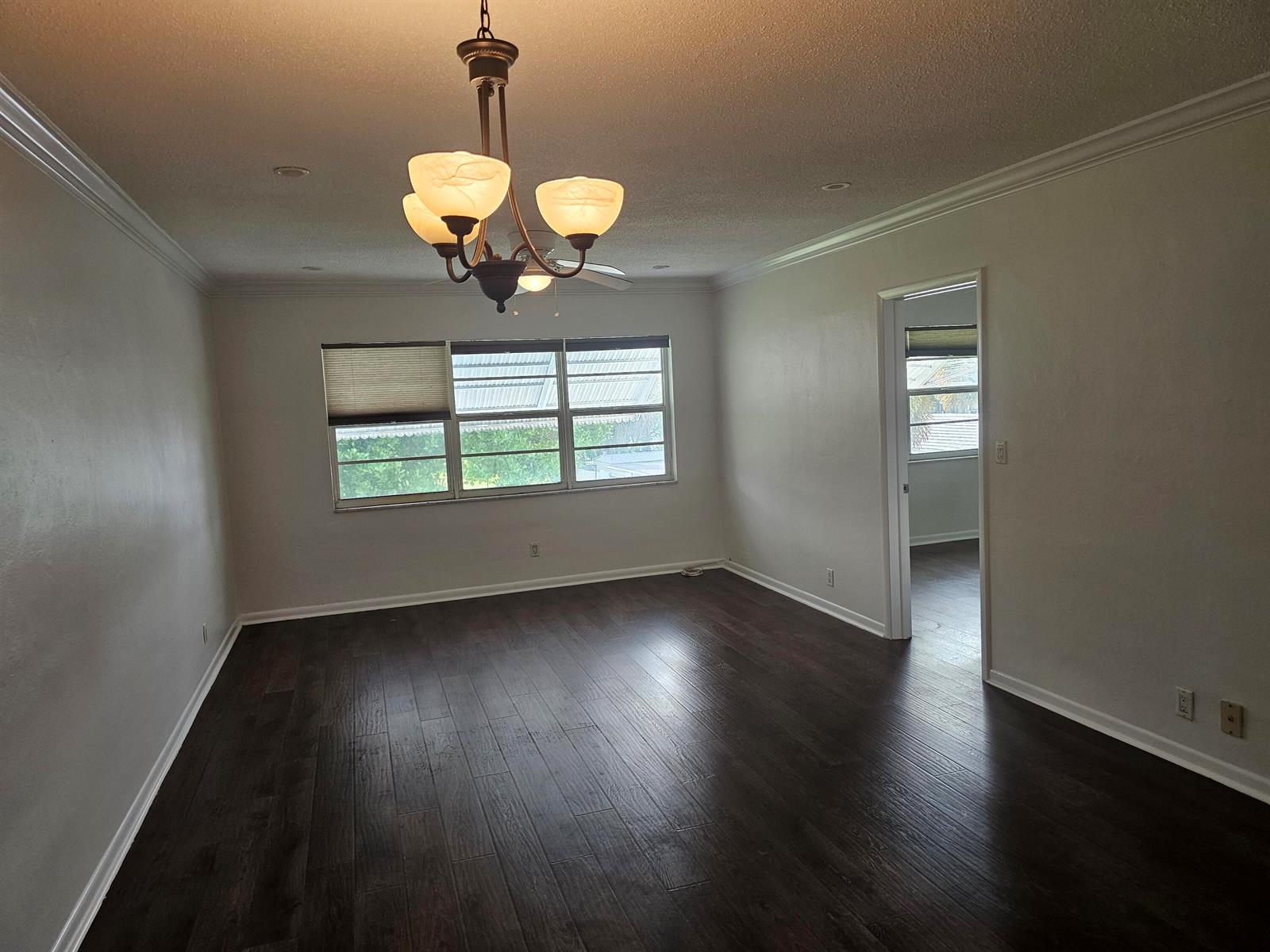 An empty room features dark wood flooring, a central chandelier, and a large window — 2851 E Golf Boulevard # 207, Pompano Beach FL 33064, POMPANO BEACH, FL