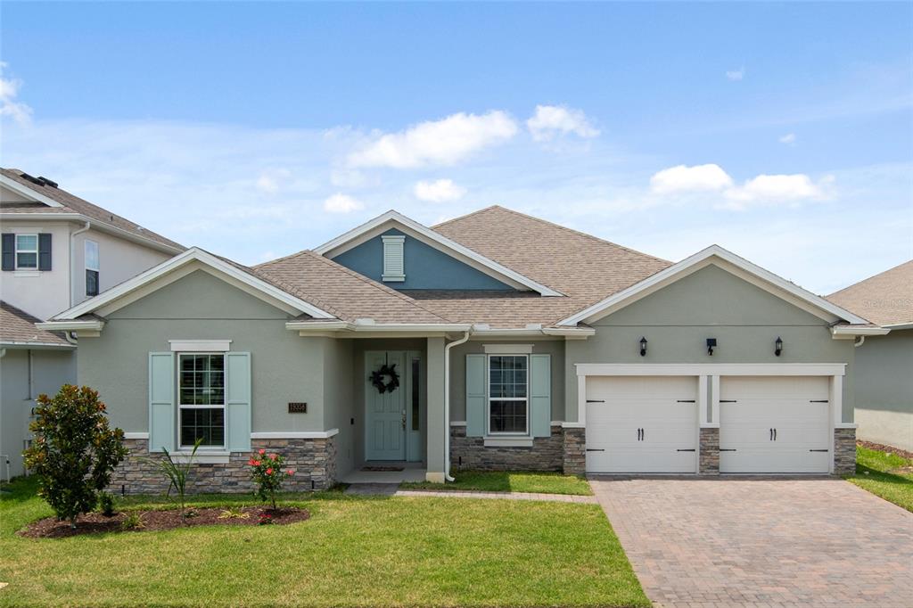 A single-story house with a two-car garage, light green stucco, and stone veneer accents — 19358 BANFIELD PLACE, ORLANDO, FL