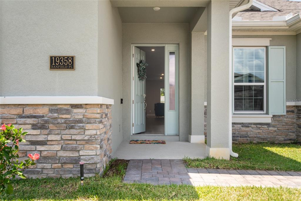 The front entrance of a house features a stone facade, a light-colored door, and a walkway — 19358 BANFIELD PLACE, ORLANDO, FL