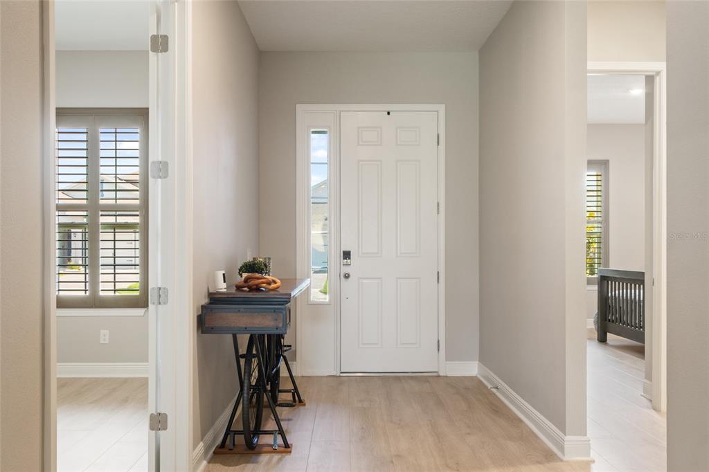 An entryway features light wood-look flooring, a white front door with a sidelight, and a vintage bicycle-base console table — 19358 BANFIELD PLACE, ORLANDO, FL