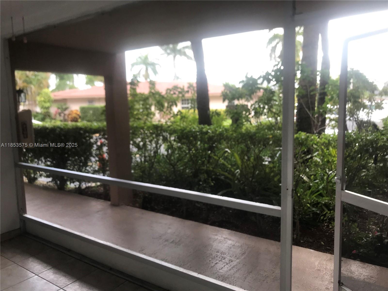 A screened-in patio overlooks a lush garden and a neighboring house — 501 Blue Heron Dr # A, Hallandale Beach FL 33009, HALLANDALE BEACH, FL