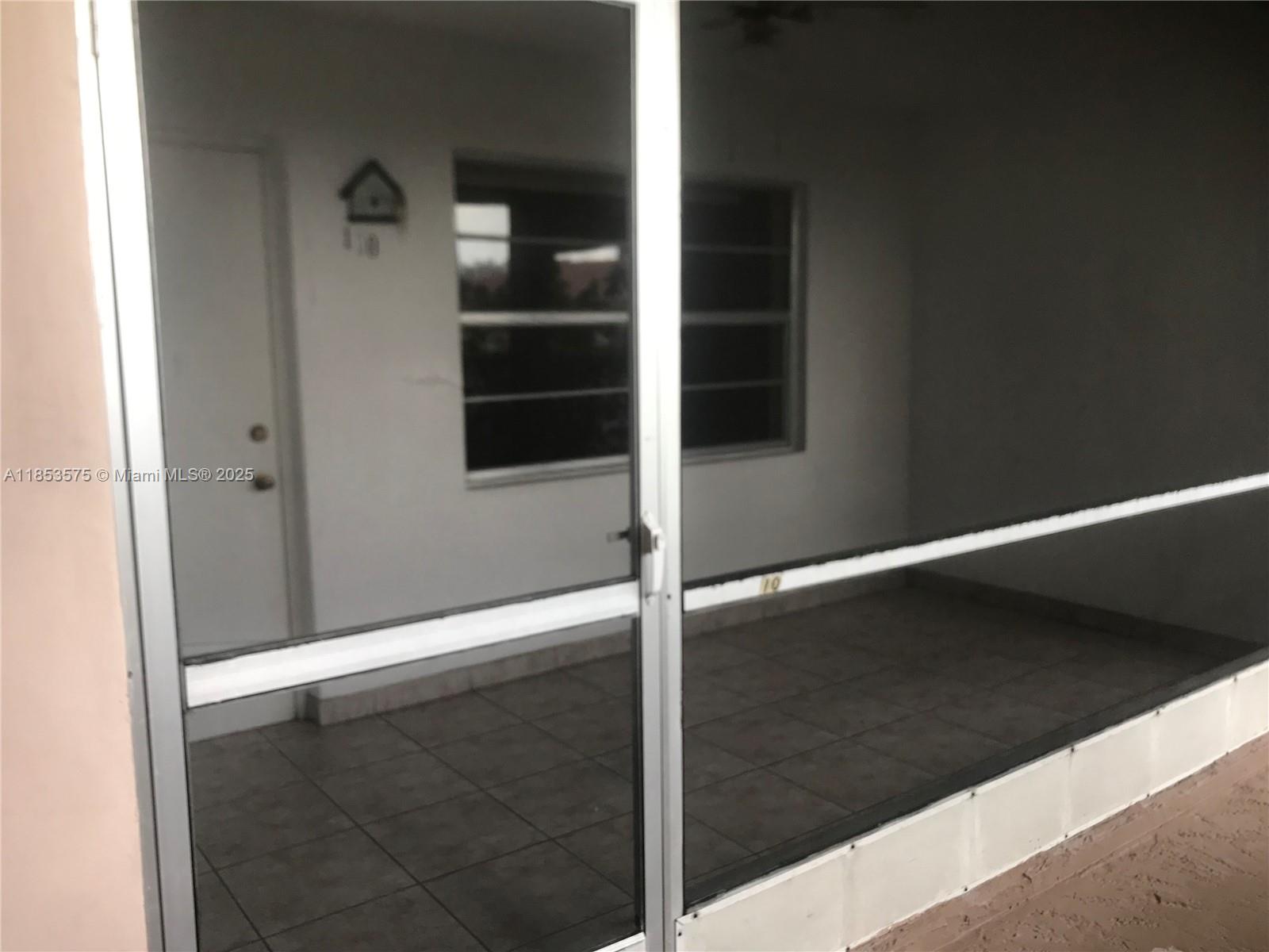 A screened-in porch features tiled flooring, a white door, and a window on the wall — 501 Blue Heron Dr # A, Hallandale Beach FL 33009, HALLANDALE BEACH, FL