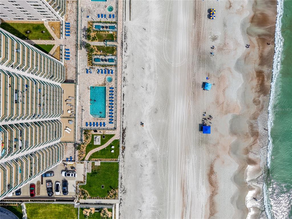 An aerial view shows a high-rise building with pools next to a sandy beach — 3315 S ATLANTIC AVENUE UNIT 1806, DAYTONA BEACH SHORES, FL