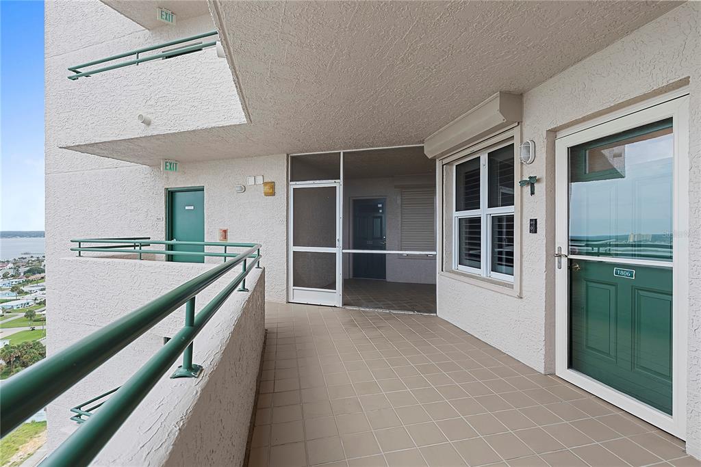 A tiled outdoor balcony features a green door, a screened enclosure, and a metal railing — 3315 S ATLANTIC AVENUE UNIT 1806, DAYTONA BEACH SHORES, FL