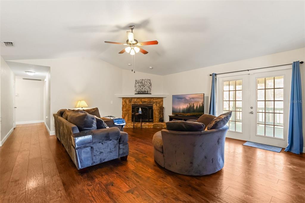 A living room features a stone fireplace, hardwood floors, a ceiling fan, and glass doors — 1922 MATTHEW COURT, LAKELAND, FL