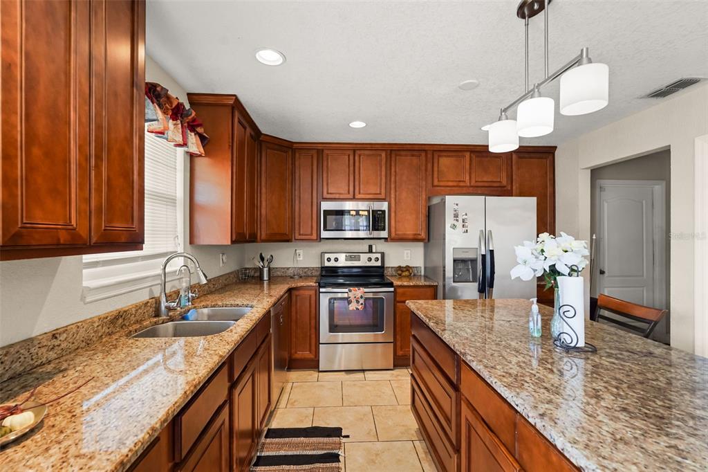 A kitchen features wood cabinets, granite countertops, stainless steel appliances, and a central island — 1922 MATTHEW COURT, LAKELAND, FL