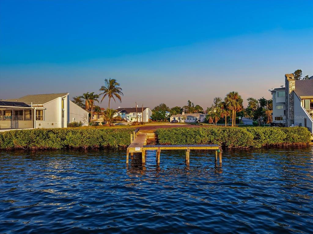 A wooden dock extends from a grassy shoreline into a body of water near houses — 2308 PALMA SOLA BOULEVARD, BRADENTON, FL