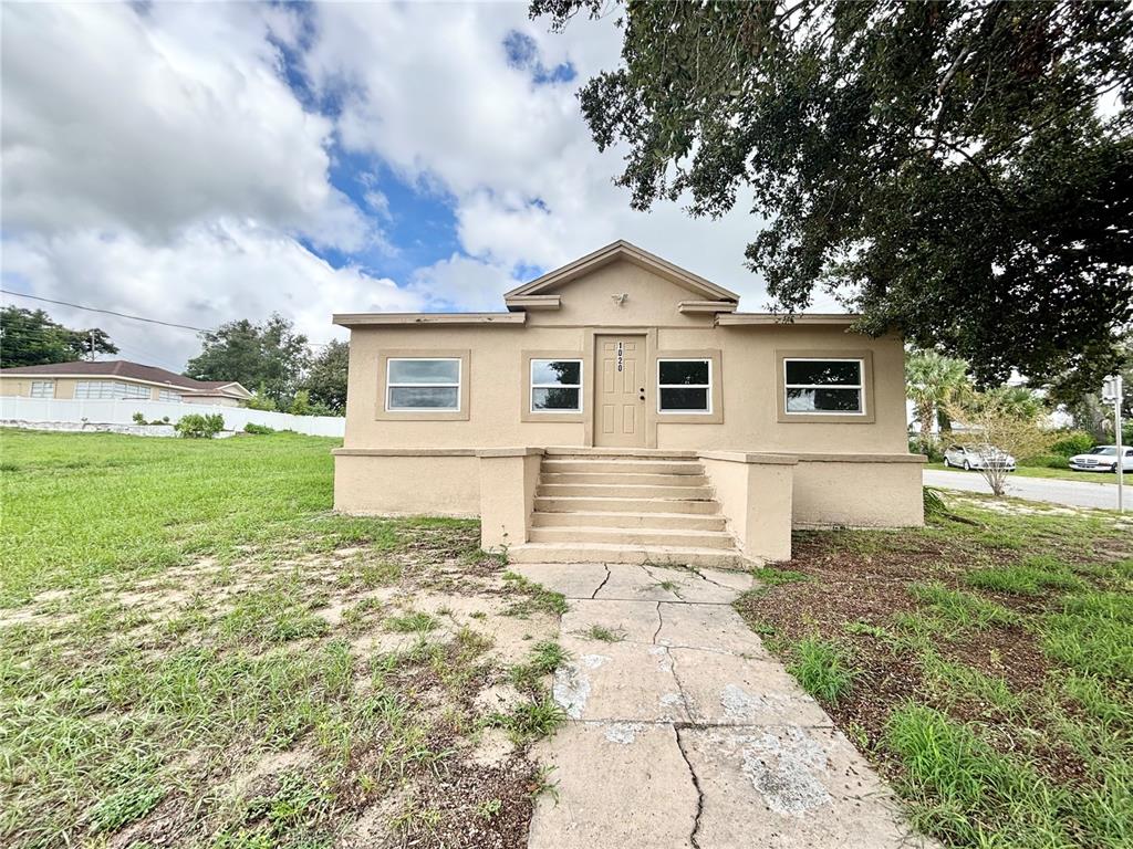 A single-story tan stucco house with a central staircase leading to the front entrance — 1020 E MAIN STREET, HAINES CITY, FL