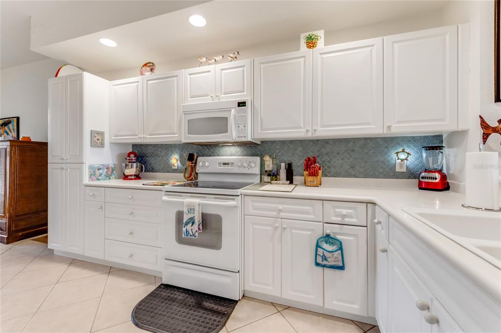A kitchen features white cabinets, a blue scalloped tile backsplash, and white appliances — 250 MINORCA BEACH WAY UNIT 203, NEW SMYRNA BEACH, FL