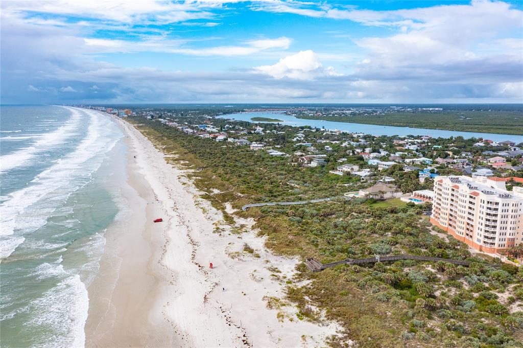 An aerial view shows a sandy beach, ocean waves, coastal vegetation, and a large residential building — 250 MINORCA BEACH WAY UNIT 203, NEW SMYRNA BEACH, FL