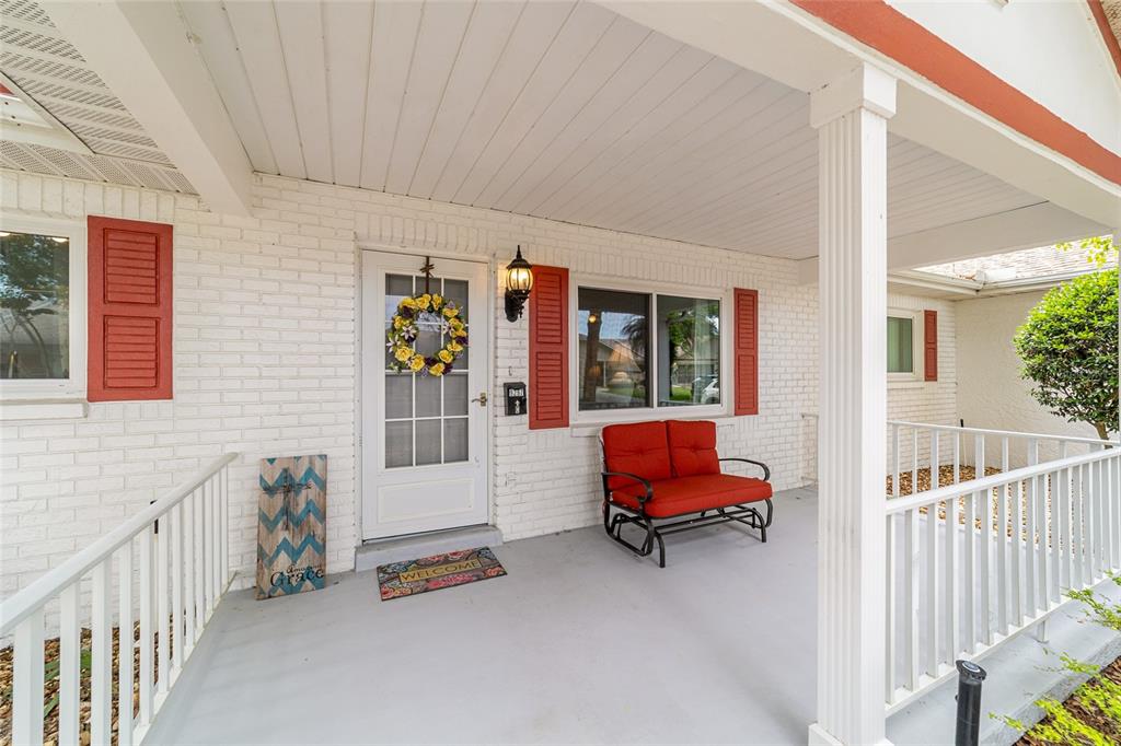 A white brick porch features a red bench, a front door with a wreath, and railings — 9297 SW 90TH COURT UNIT C, OCALA, FL