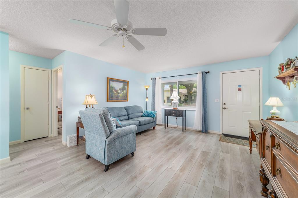 A living room with light blue walls, wood-look flooring, a ceiling fan, and a sofa — 9297 SW 90TH COURT UNIT C, OCALA, FL