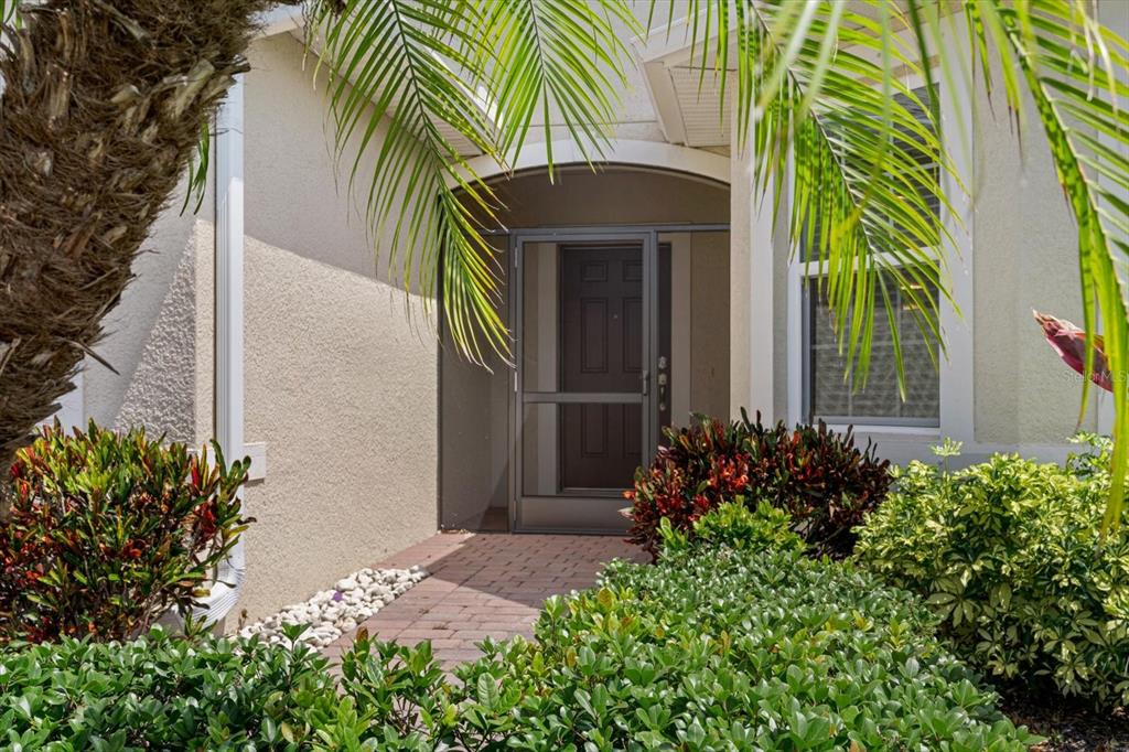 A brick walkway leads to a front entrance with a screen door and landscaping — 8932 EXCELSIOR PLACE, VENICE, FL
