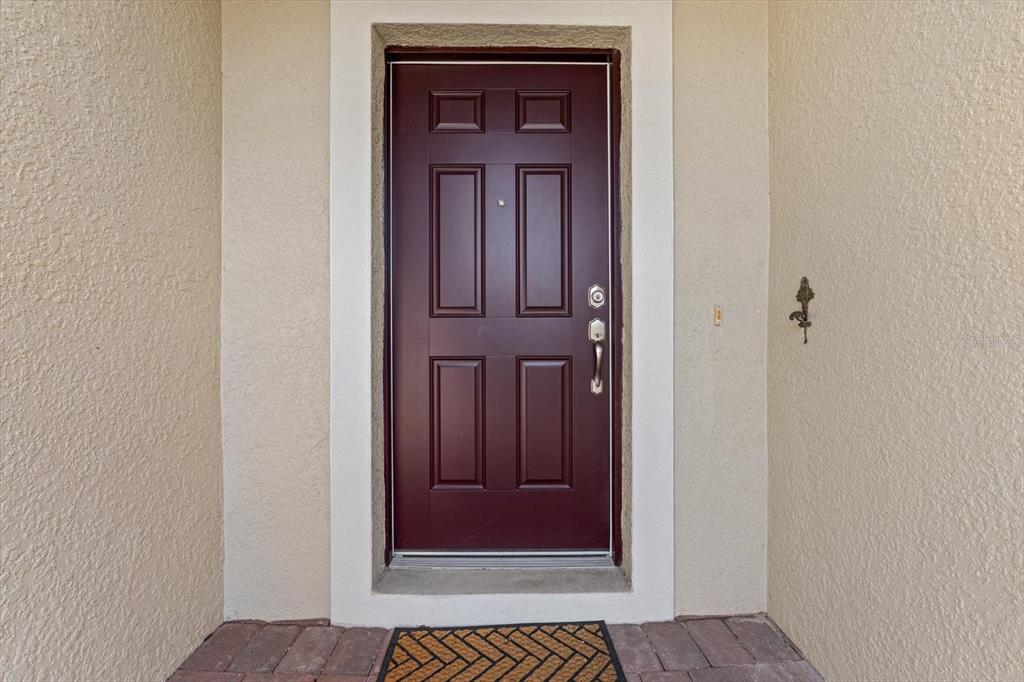 A dark red front door with a white frame is set into a beige stucco wall — 8932 EXCELSIOR PLACE, VENICE, FL