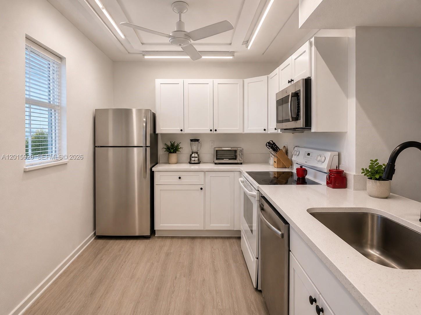 A kitchen features white cabinetry, stainless steel appliances, light wood flooring, and a ceiling fan — 14170 SW 84th St # F, Miami FL 33183, MIAMI, FL