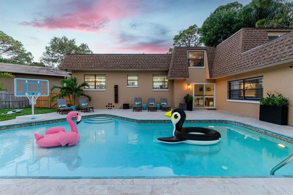 A backyard swimming pool with two large inflatable floats sits behind a two-story house — 14389 83RD PLACE, SEMINOLE, FL