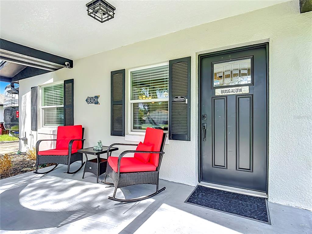 A covered porch features two red rocking chairs, a small table, and a black door — 623 JERSEY AVENUE, ST CLOUD, FL