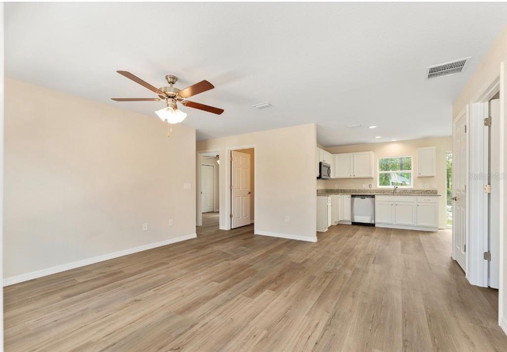 An open-concept living area with light wood-look flooring, a ceiling fan, and an adjacent kitchen — 467 SW ALVAREZ ROAD, DUNNELLON, FL