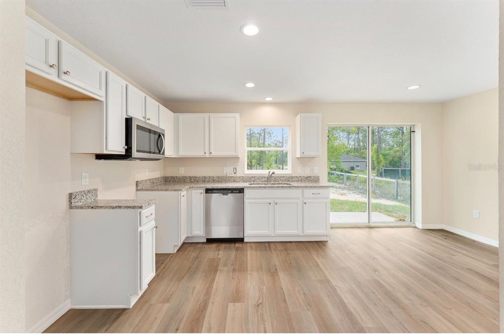 A kitchen with white cabinets, granite countertops, stainless steel appliances, and wood-look flooring — 467 SW ALVAREZ ROAD, DUNNELLON, FL