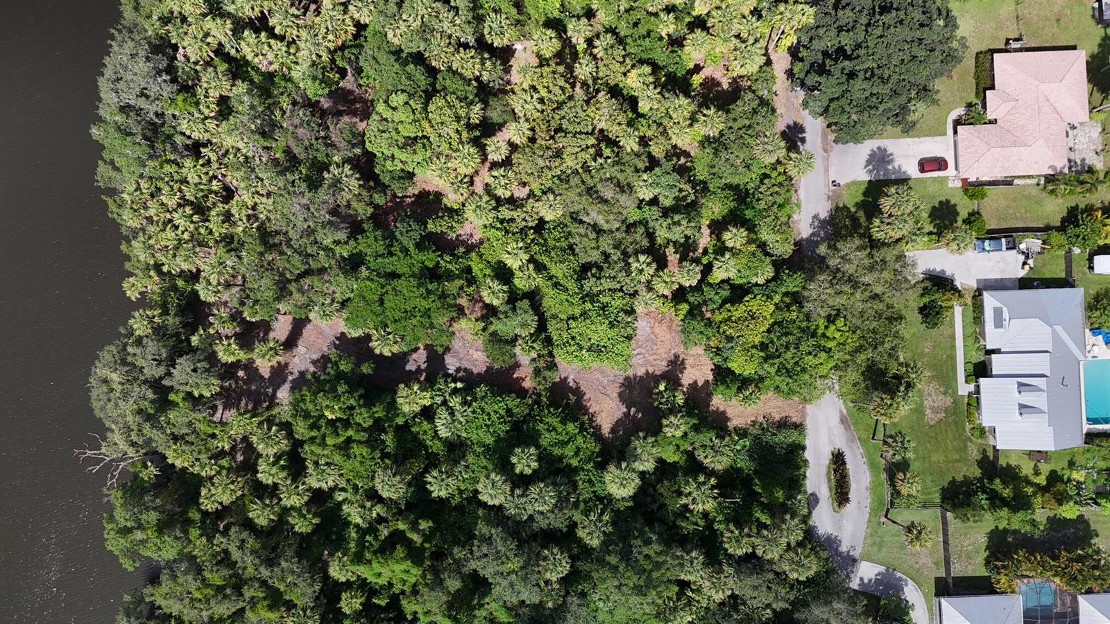 An aerial view shows a wooded lot bordering a river next to residential houses — 14560 SW Sonora Terrace, FL 34956, FL