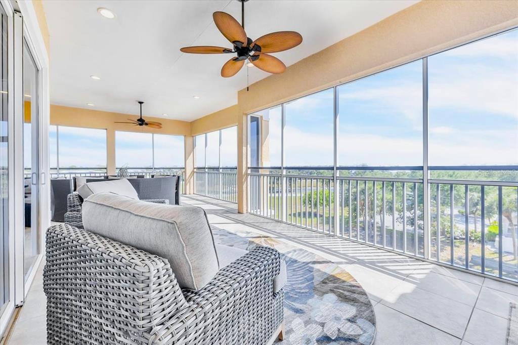 A screened-in balcony features wicker furniture, ceiling fans, and a view of the outdoors — 8560 AMBERJACK CIRCLE UNIT 301, ENGLEWOOD, FL
