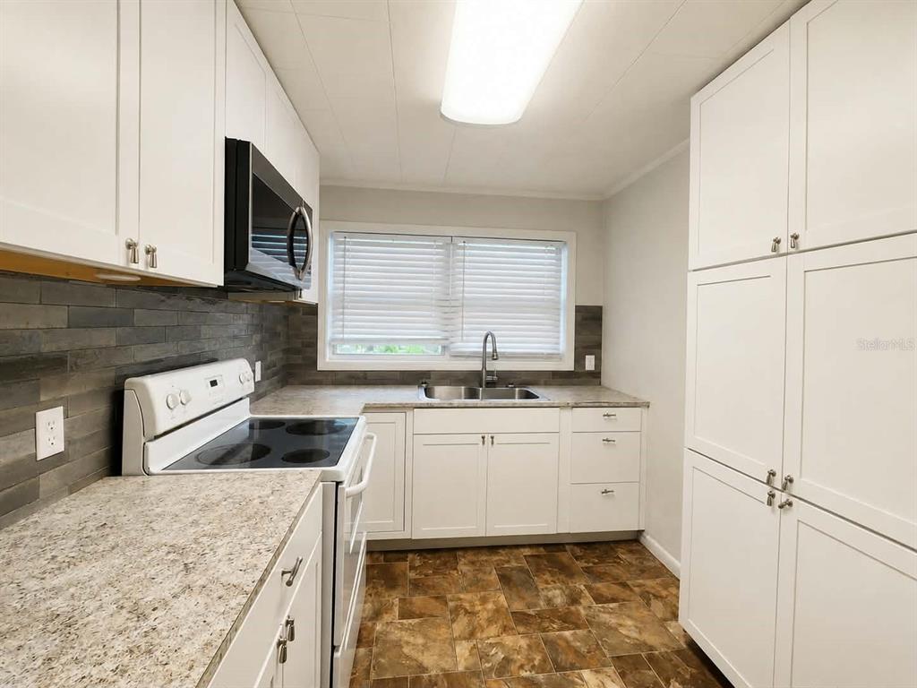 A kitchen features white cabinets, a granite-look countertop, a black microwave, and a tiled backsplash — 108 9TH ELOISE STREET, WINTER HAVEN, FL
