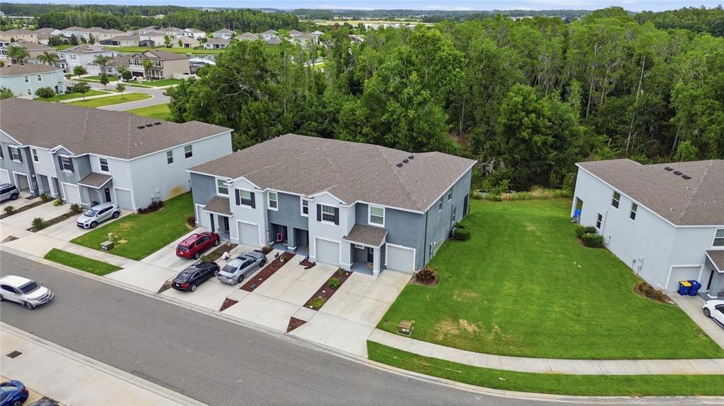 An aerial view shows two-story townhomes with driveways and a large grassy side yard — 32825 PEZ LANDING LANE, WESLEY CHAPEL, FL