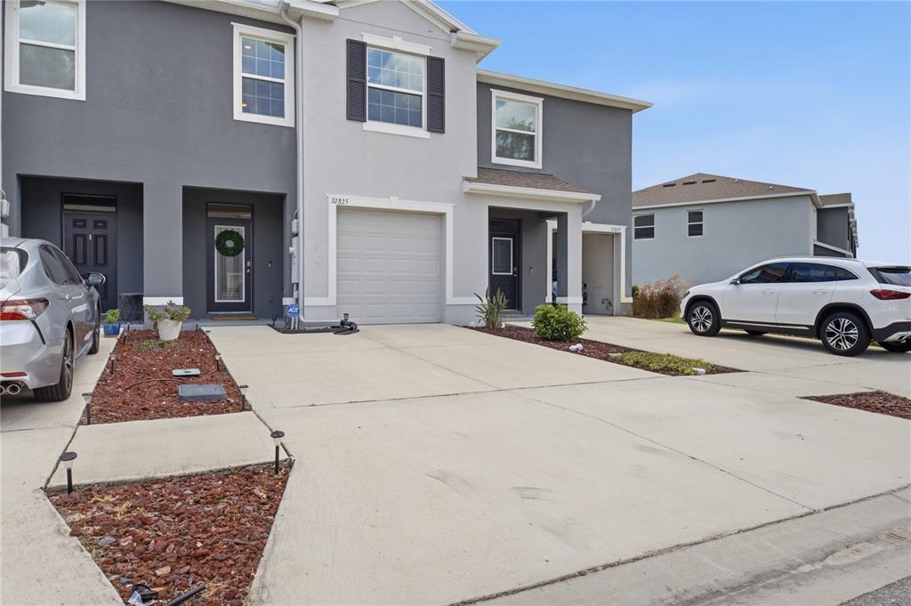 A two-story townhouse exterior features a concrete driveway, a garage, and a small front yard — 32825 PEZ LANDING LANE, WESLEY CHAPEL, FL