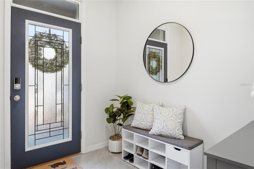 An entryway features a dark blue front door, a white shoe bench, and a round mirror — 32825 PEZ LANDING LANE, WESLEY CHAPEL, FL