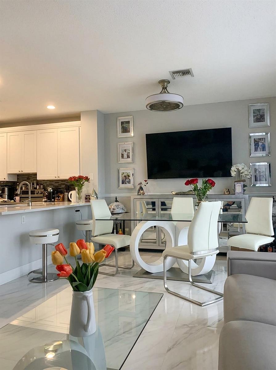 A modern dining area with a glass table, white chairs, and a wall-mounted television — 7862 Sienna Springs Drive, Lake Worth FL 33463, LAKE WORTH, FL