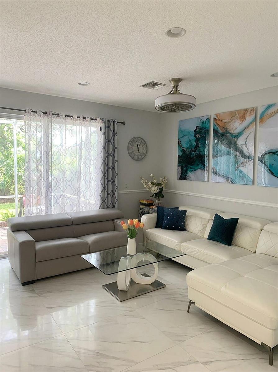 A living room features a white sectional, a grey sofa, glass coffee table, and abstract art — 7862 Sienna Springs Drive, Lake Worth FL 33463, LAKE WORTH, FL