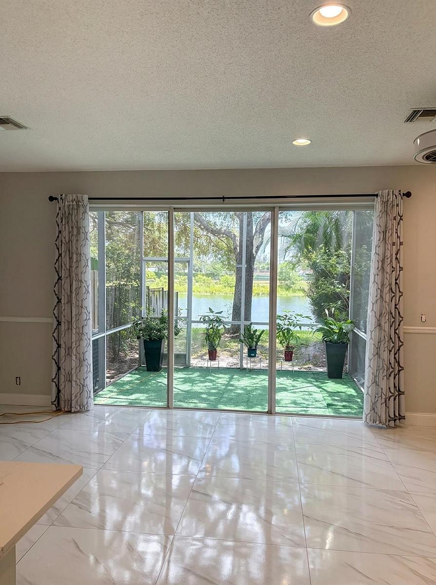 A room with white marble-look tile floors overlooks a screened-in patio and a lake — 7862 Sienna Springs Drive, Lake Worth FL 33463, LAKE WORTH, FL