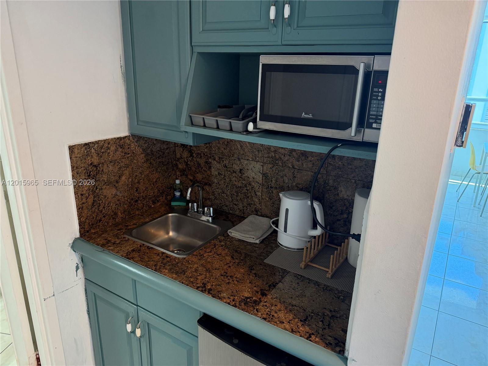 A small kitchenette features teal cabinets, a granite countertop, a sink, and a microwave — 5445 Collins Ave # 1606, Miami Beach FL 33140, MIAMI BEACH, FL