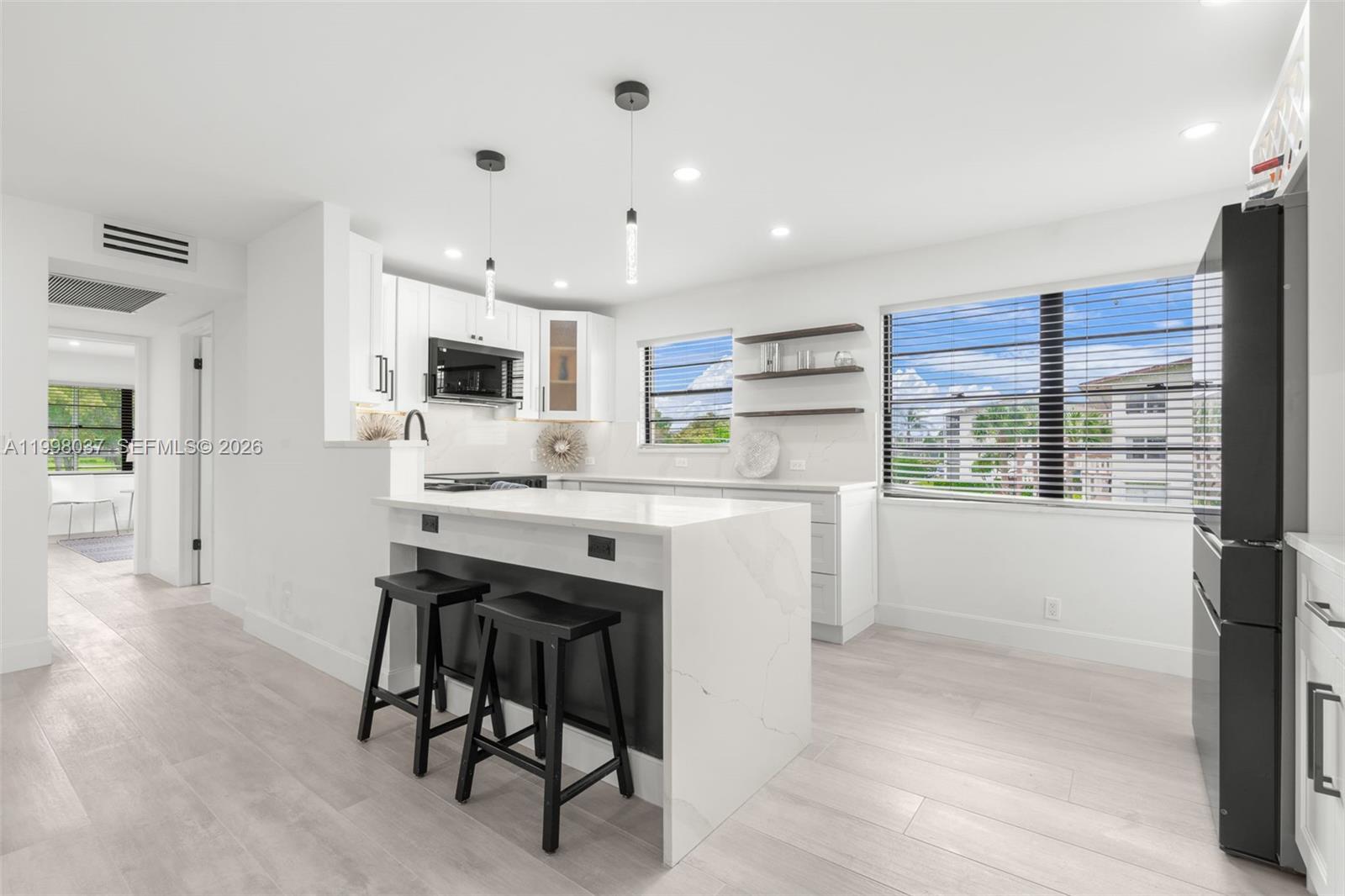 A modern kitchen features white cabinetry, a black refrigerator, and a dark wood island — 319 Preston H # 319, Boca Raton FL 33434, BOCA RATON, FL