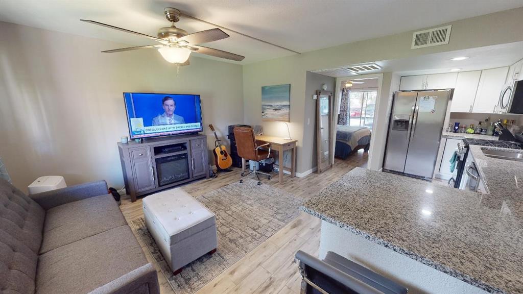 A living room with a television, desk, and kitchen area featuring granite countertops and stainless appliances — 133 OYSTER BAY CIRCLE UNIT 100, ALTAMONTE SPRINGS, FL